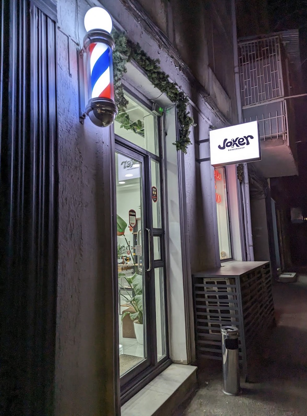JOKER Barbershop entrance at night with illuminated barber pole
